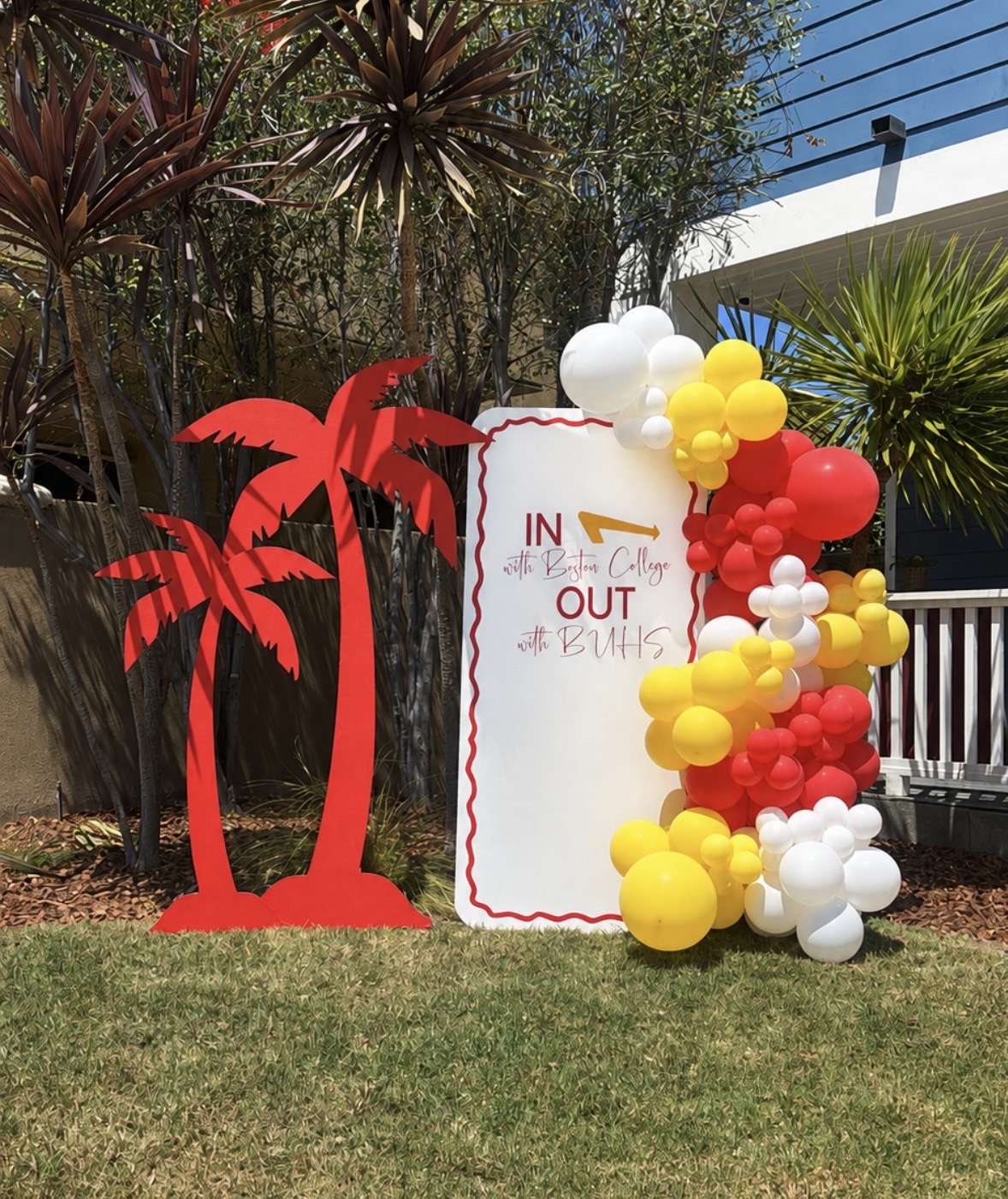 Real install — maroon, gold and white graduation sign with palm cutouts and organic garland